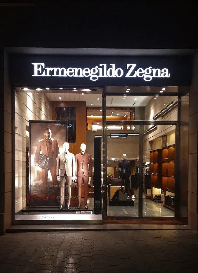 Фасад бутика Ermenegildo Zegna с подсвеченной вывеской и витриной с костюмами ночью