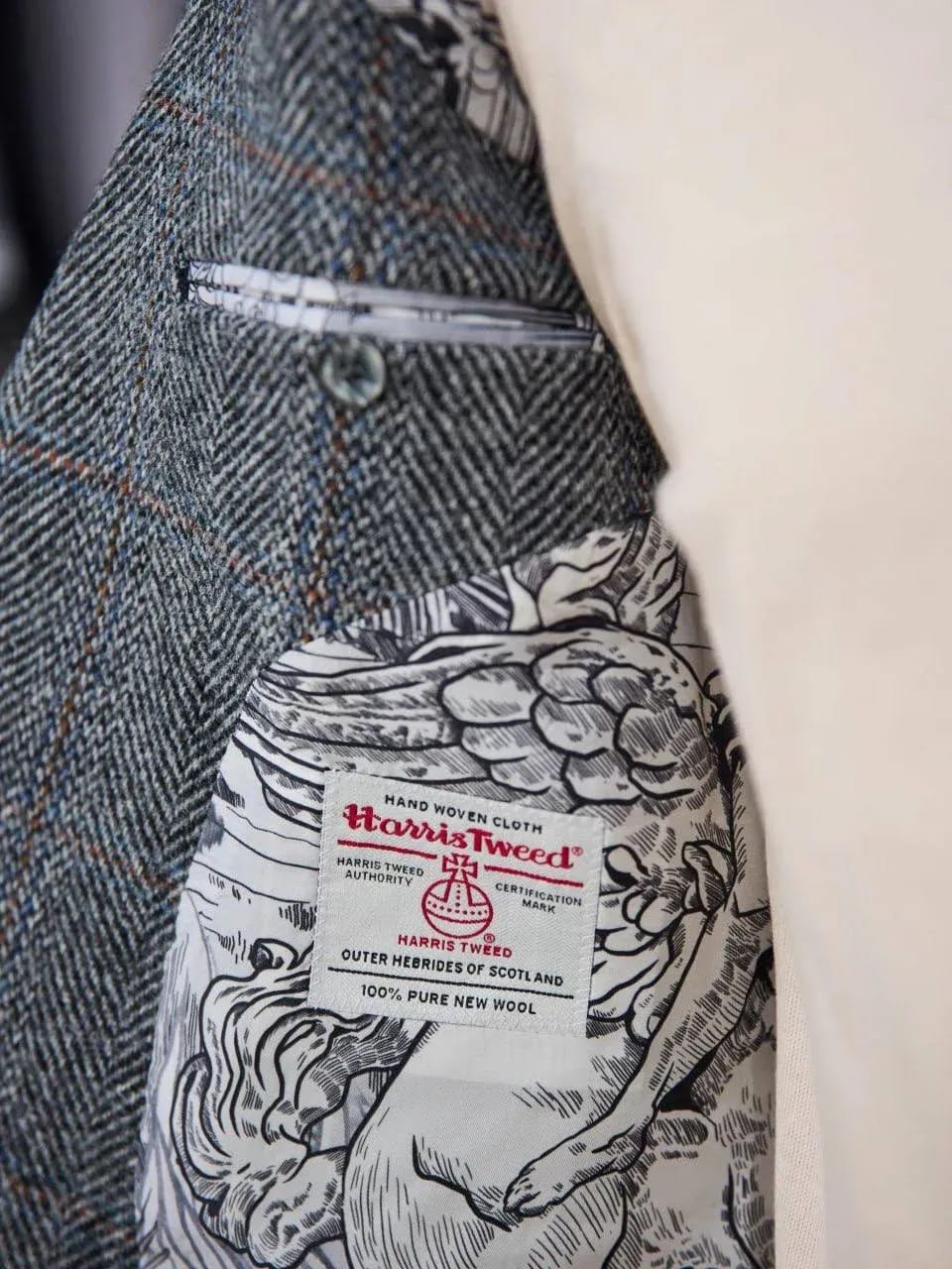 Крупный план шильдика Harris Tweed на подкладке серого твидового пиджака — круглый логотип бренда с текстом «Outer Hebrides of Scotland, 100% Pure New Wool».