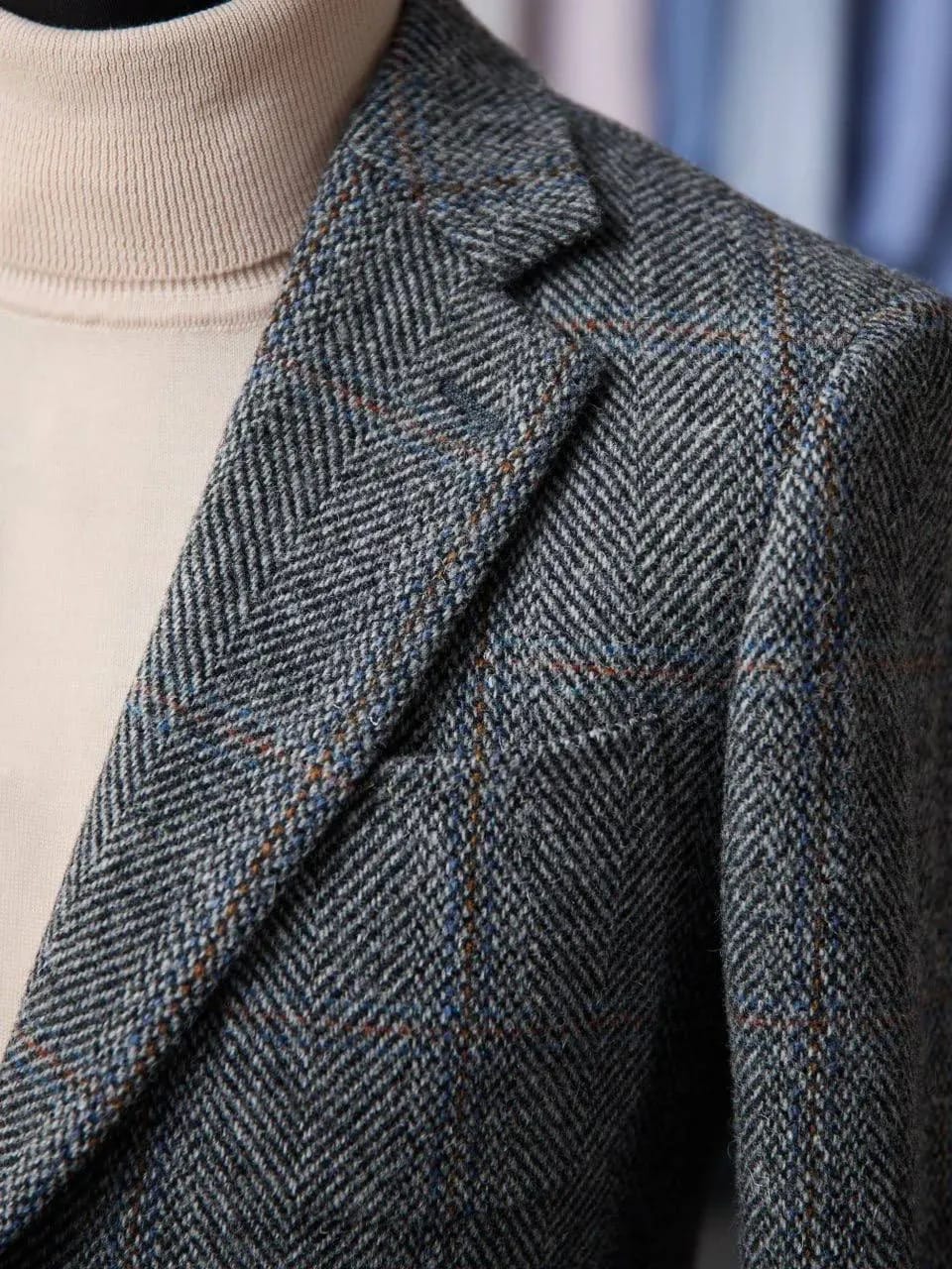 Крупный план левого лацкана и нагрудного кармана серого пиджака из Harris Tweed — чётко видна фактура ткани «ёлочка» с рыжими вкраплениями.