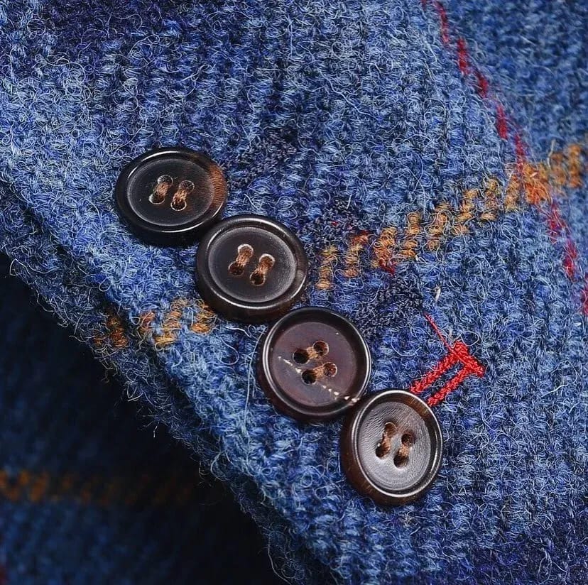 Крупный план пуговиц на синем клетчатом пальто из Harris Tweed: четыре тёмные роговые пуговицы, красные и рыжие нити клетки
