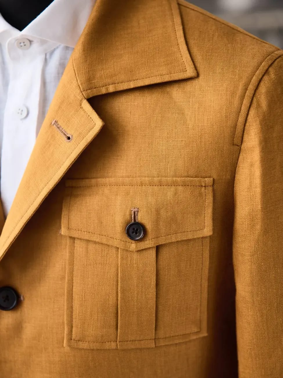 Горчичный льняной пиджак-сафари с нагрудным накладным карманом и тёмными пуговицами крупным планом