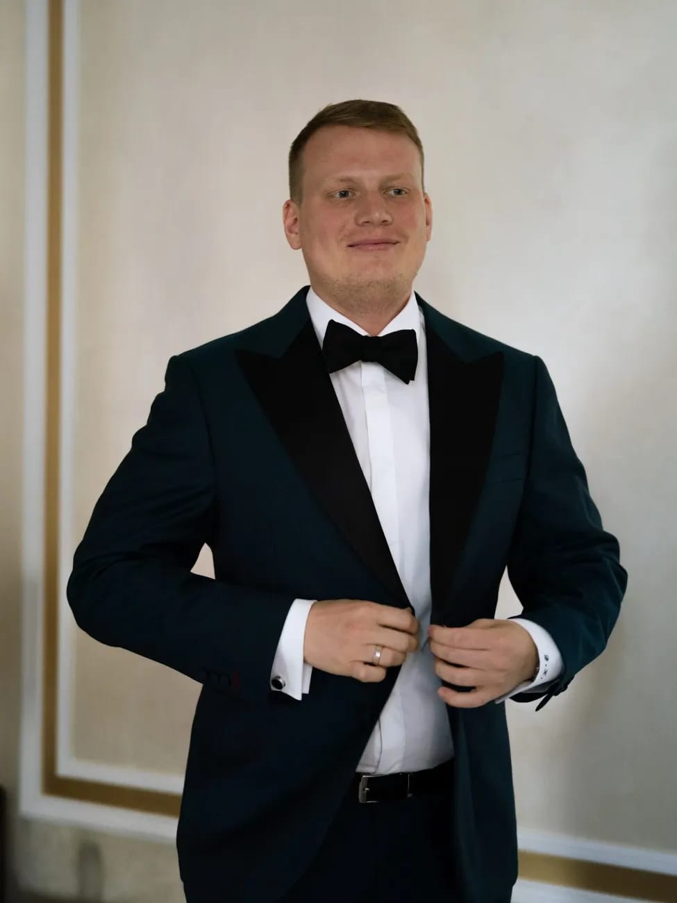 Мужчина застёгивает тёмно-синий смокинг с чёрным атласным лацканом и бабочкой на торжестве