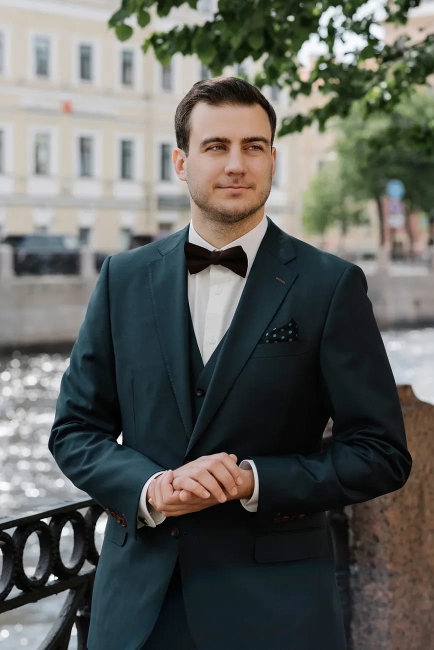 Жених в тёмно-зелёном костюме-тройке с бордовой бабочкой на набережной